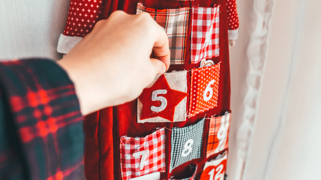 Dziecko wyciąga karteczkę z materiałowego kalendarza adwentowego — rodzinny rytuał odkrywania zadań.